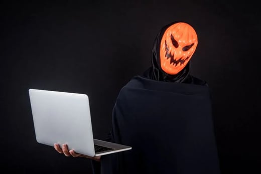 Person wearing a pumpkin mask and hoodie using a laptop, representing scam prevention tips.