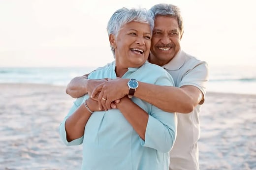 Happy older couple hugging on a beach, representing retirement planning